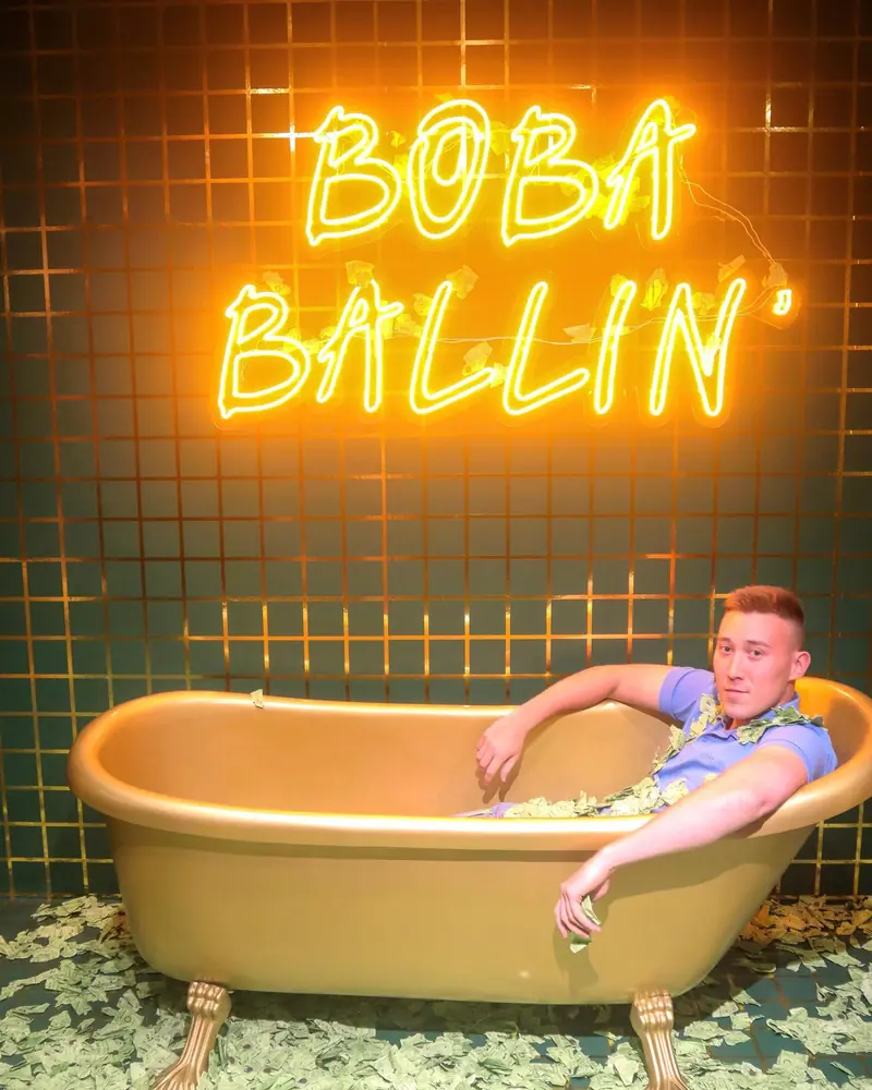 Arthur lounging in a bathtub under a neon Boba Ballin' sign