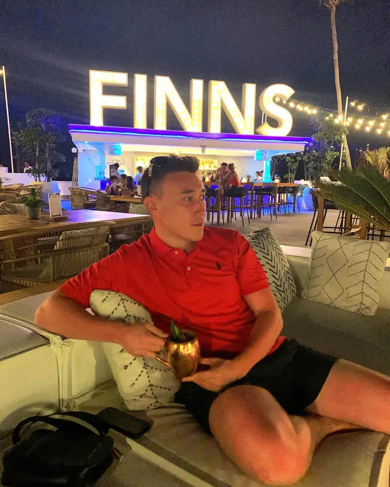 Arthur relaxing on a lounge sofa in front of the lit Finns sign at night
