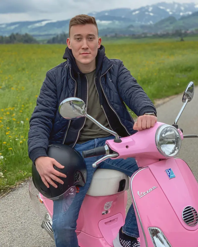 Arthur on a pink Vespa in an alpine meadow