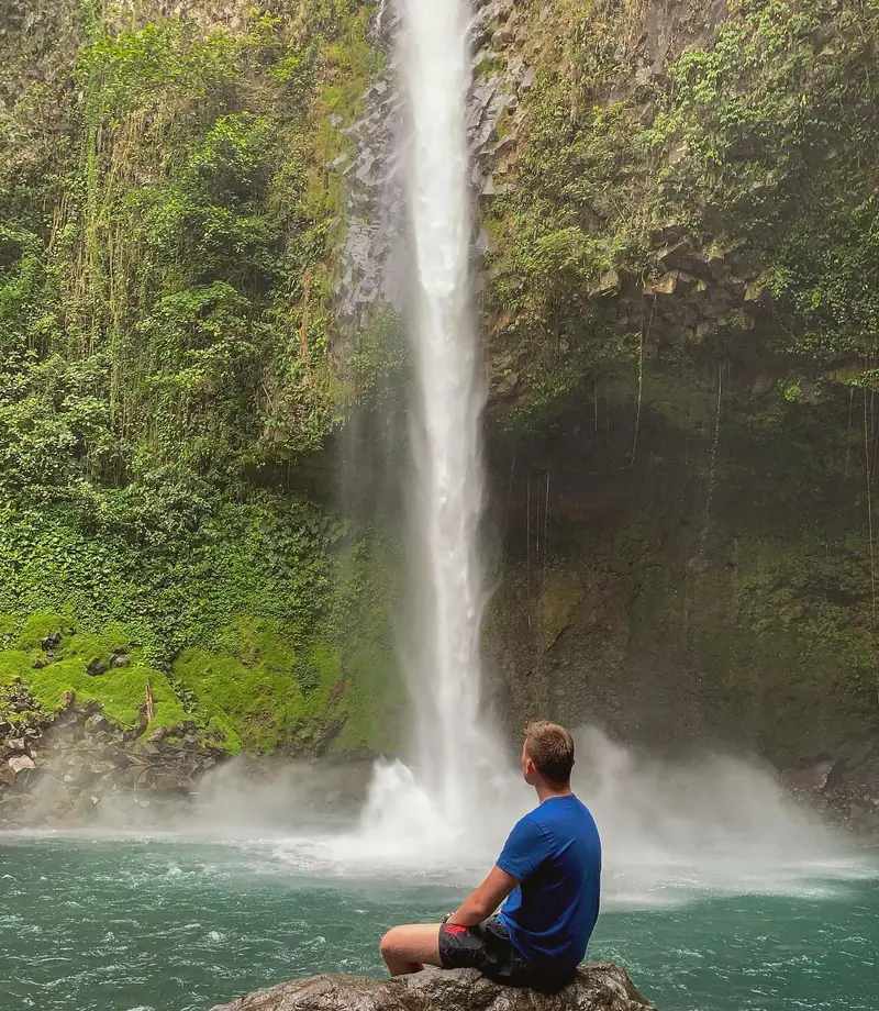 Arthur sitting on a rock in front of a jungle waterfall
